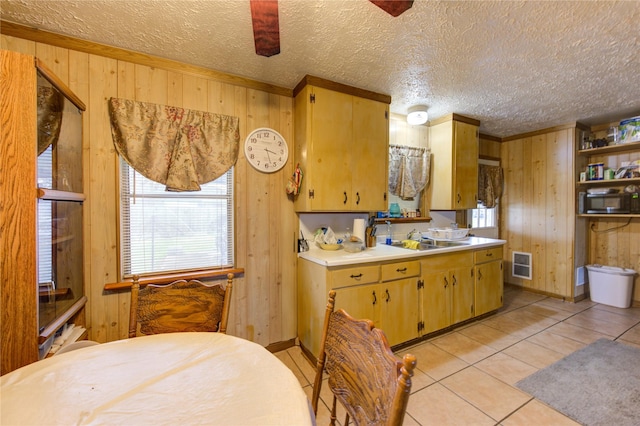 kitchen featuring sink, light tile patterned floors, wooden walls, and a textured ceiling