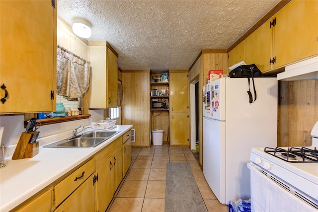 kitchen with sink, white appliances, a textured ceiling, light tile patterned flooring, and wood walls