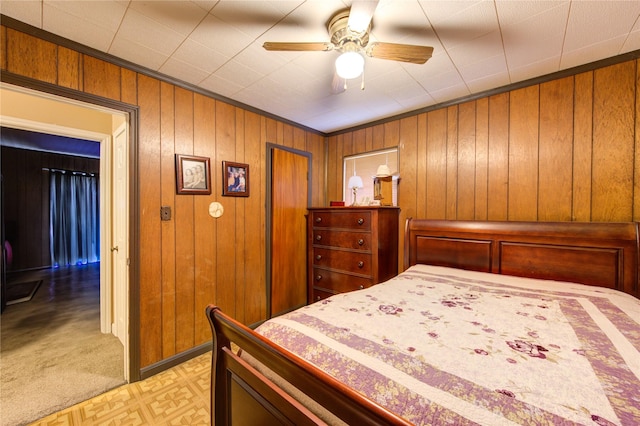 bedroom with ornamental molding, ceiling fan, wooden walls, and a closet