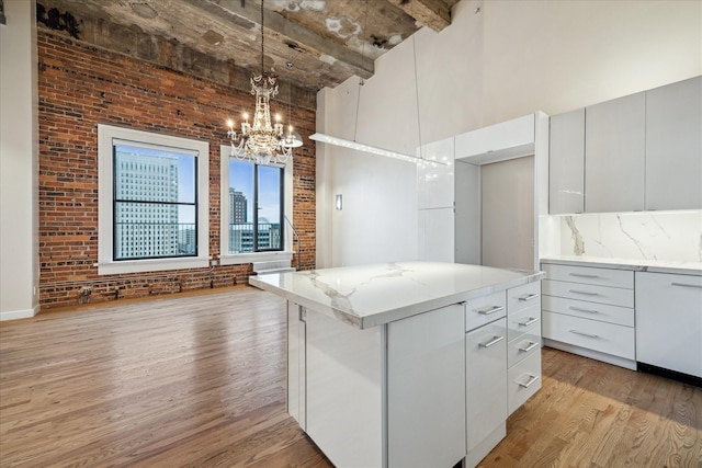 kitchen featuring hanging light fixtures, brick wall, a kitchen island, and white cabinets