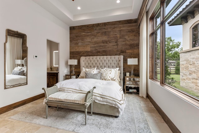 bedroom featuring a tray ceiling, ensuite bath, and wood walls