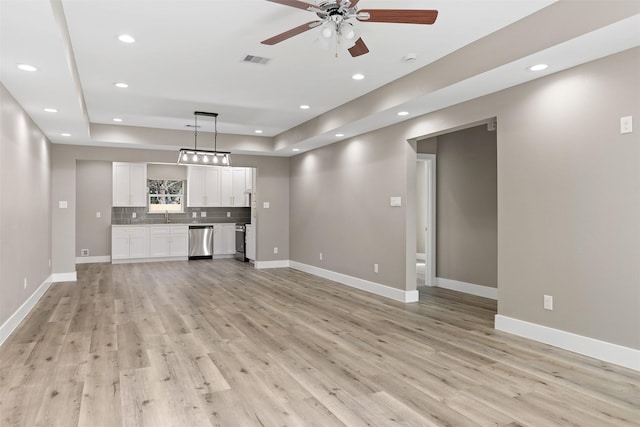 unfurnished living room featuring a raised ceiling, ceiling fan, sink, and light hardwood / wood-style floors