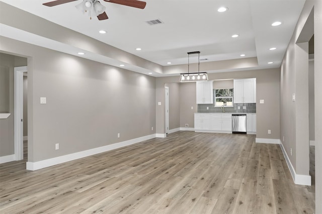 unfurnished living room with sink, a tray ceiling, light hardwood / wood-style floors, and ceiling fan