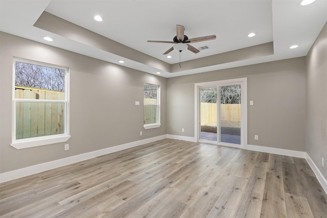empty room featuring a tray ceiling, ceiling fan, and light wood-type flooring