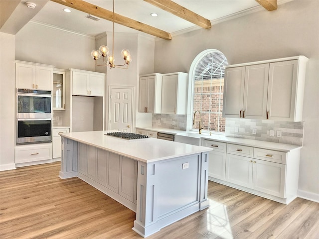 kitchen featuring light wood finished floors, appliances with stainless steel finishes, beamed ceiling, and white cabinetry