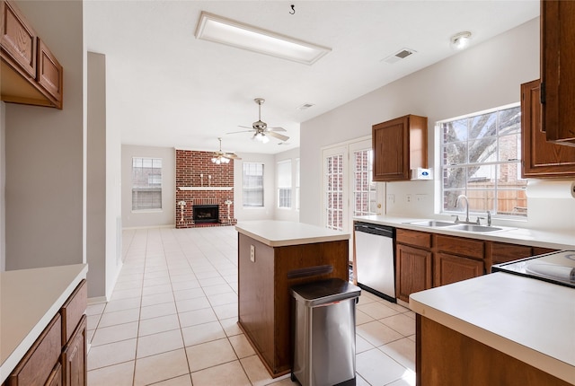 kitchen featuring light tile patterned floors, stainless steel dishwasher, a fireplace, a kitchen island, and sink