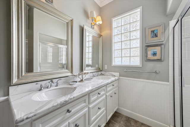 full bathroom with double vanity, a wainscoted wall, a sink, and tiled shower