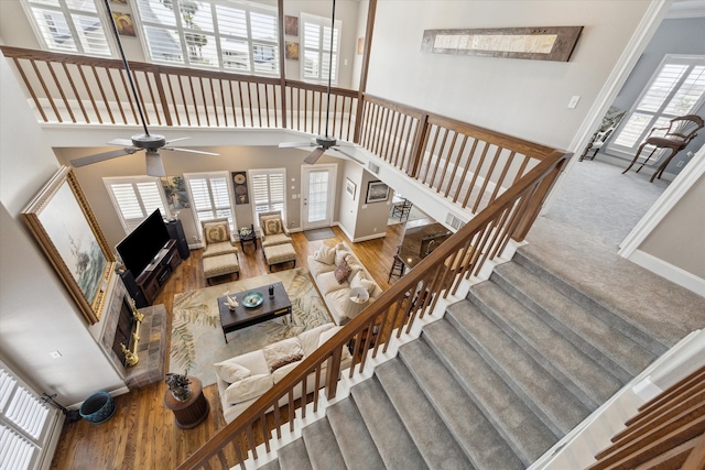 living area with wood finished floors, a ceiling fan, a towering ceiling, stairs, and baseboards