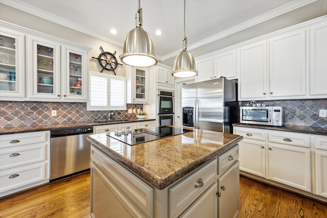 kitchen with stainless steel appliances, wood finished floors, a kitchen island, ornamental molding, and pendant lighting