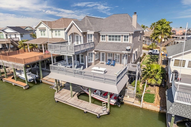 rear view of house featuring a shingled roof, a chimney, a water view, and a residential view