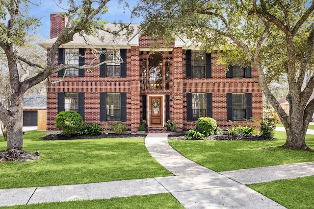 view of front of property featuring a front lawn, a chimney, and brick siding