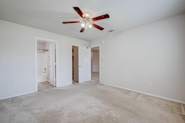 unfurnished bedroom featuring ensuite bath, light colored carpet, ceiling fan, and a textured ceiling