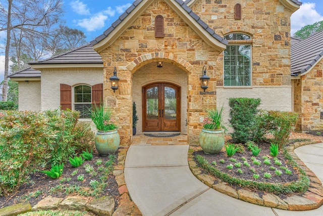 view of exterior entry featuring stone siding, brick siding, and french doors