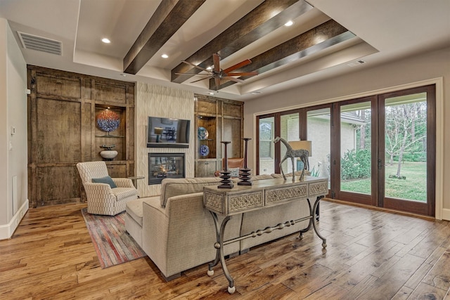 living room featuring beam ceiling, a fireplace, recessed lighting, visible vents, and light wood-type flooring