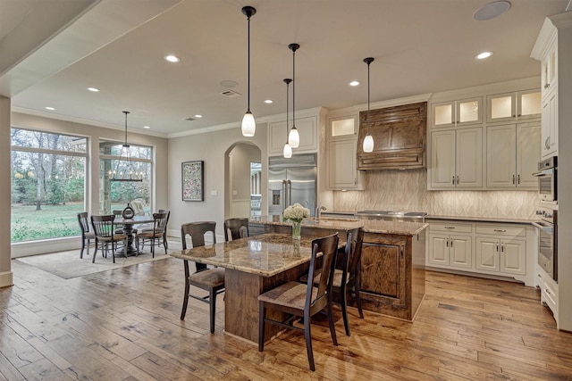 dining space featuring arched walkways, ornamental molding, recessed lighting, and light wood-style floors