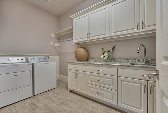 clothes washing area featuring cabinet space, washing machine and dryer, baseboards, and a sink