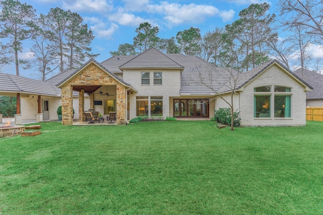 rear view of property featuring an outdoor fire pit, a patio, stone siding, ceiling fan, and a yard