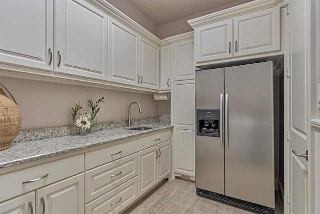 kitchen with stainless steel fridge, light stone countertops, wood tiled floor, white cabinetry, and a sink