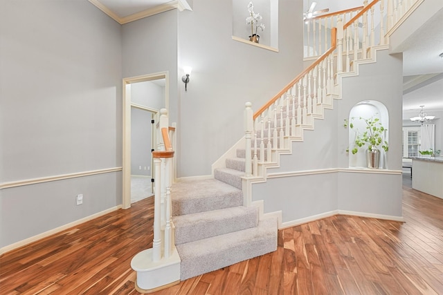 staircase with crown molding, a towering ceiling, baseboards, and wood finished floors