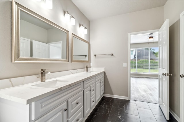 full bath with marble finish floor, a sink, baseboards, and double vanity