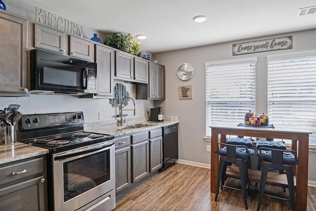 kitchen featuring dark hardwood / wood-style flooring, black appliances, light stone countertops, sink, and decorative backsplash