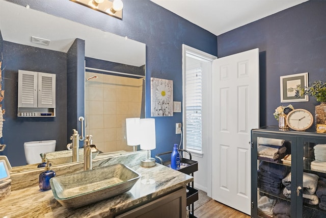 bathroom featuring hardwood / wood-style floors, tiled shower, vanity, and toilet