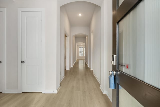 corridor featuring arched walkways, light wood-style flooring, and baseboards