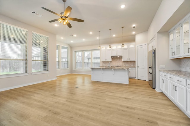 kitchen featuring visible vents, white cabinets, glass insert cabinets, light stone counters, and freestanding refrigerator