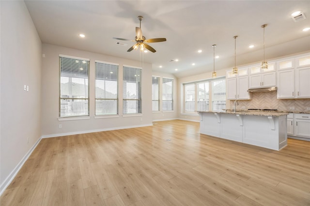 kitchen featuring a center island with sink, white cabinets, glass insert cabinets, a kitchen breakfast bar, and open floor plan