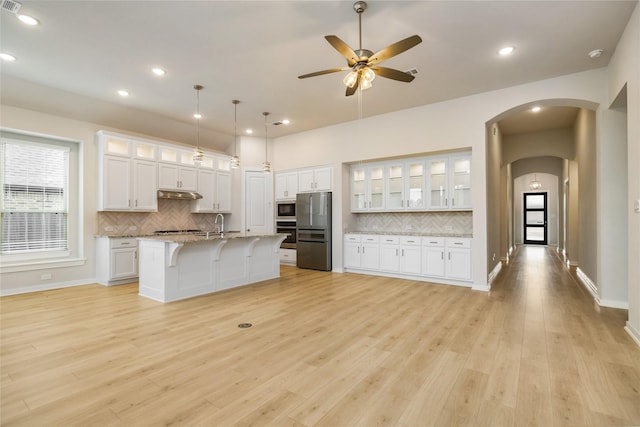 kitchen with a center island with sink, white cabinets, glass insert cabinets, appliances with stainless steel finishes, and under cabinet range hood