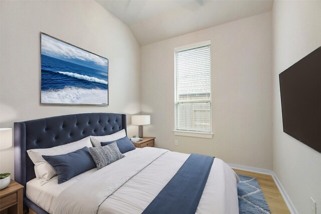 bedroom featuring lofted ceiling, baseboards, and light wood finished floors