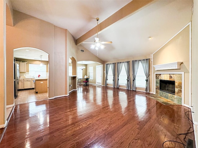 unfurnished living room featuring a tile fireplace, ceiling fan, hardwood / wood-style floors, beam ceiling, and high vaulted ceiling