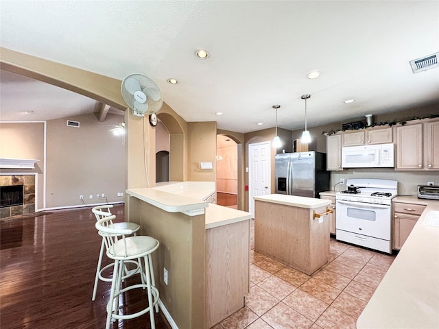 kitchen featuring a center island, a kitchen breakfast bar, pendant lighting, white appliances, and a tiled fireplace