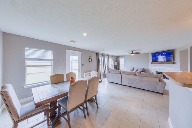 dining space featuring light tile patterned floors, a fireplace, a textured ceiling, and ceiling fan