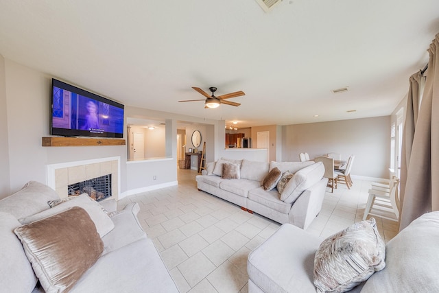 tiled living room with a tile fireplace and ceiling fan