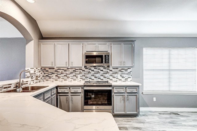 kitchen with appliances with stainless steel finishes, tasteful backsplash, sink, gray cabinetry, and light stone countertops