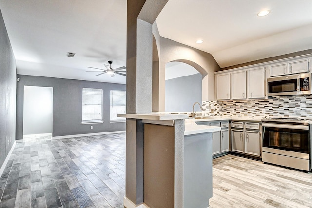 kitchen featuring sink, tasteful backsplash, light wood-type flooring, kitchen peninsula, and stainless steel appliances