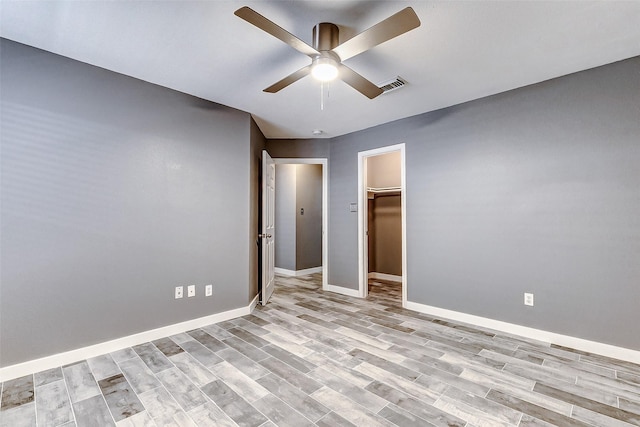 unfurnished bedroom with ceiling fan, a walk in closet, a closet, and light wood-type flooring