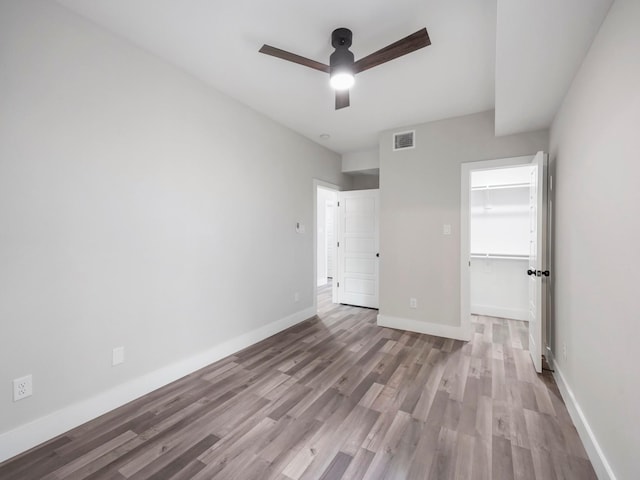 unfurnished bedroom featuring ceiling fan, a walk in closet, light hardwood / wood-style floors, and a closet