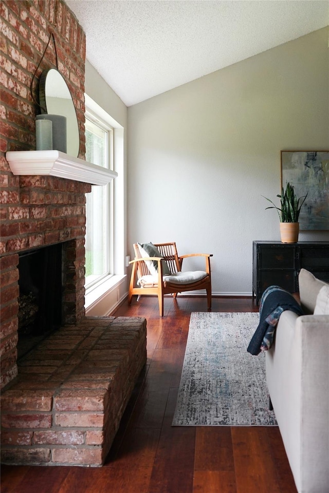 living area with a brick fireplace, lofted ceiling, dark hardwood / wood-style flooring, and a textured ceiling