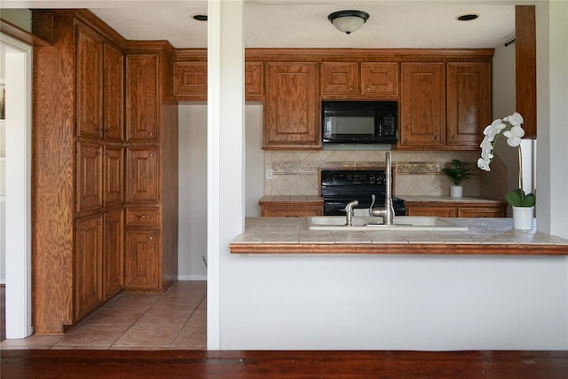 kitchen featuring light tile patterned floors, stove, kitchen peninsula, tile counters, and tasteful backsplash