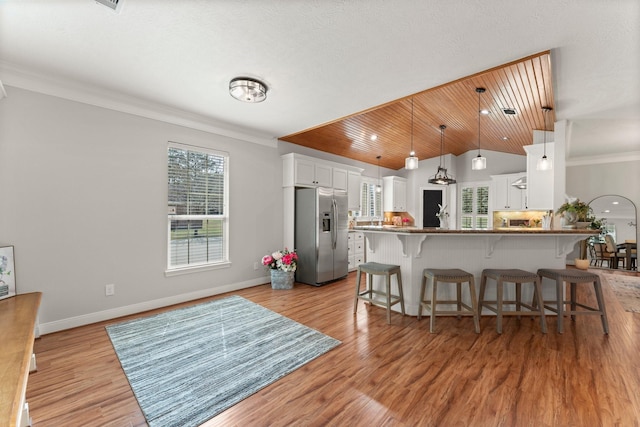 kitchen with ornamental molding, white cabinets, stainless steel fridge with ice dispenser, decorative light fixtures, and light wood-type flooring