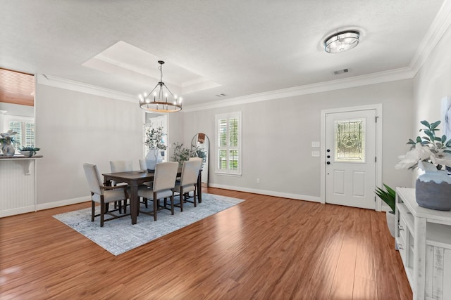 dining space with crown molding, a notable chandelier, light hardwood / wood-style floors, and a tray ceiling