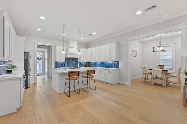 kitchen with stainless steel refrigerator, hanging light fixtures, white cabinets, a center island with sink, and custom exhaust hood