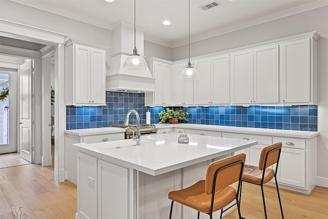 kitchen with white cabinetry, an island with sink, light hardwood / wood-style flooring, and pendant lighting