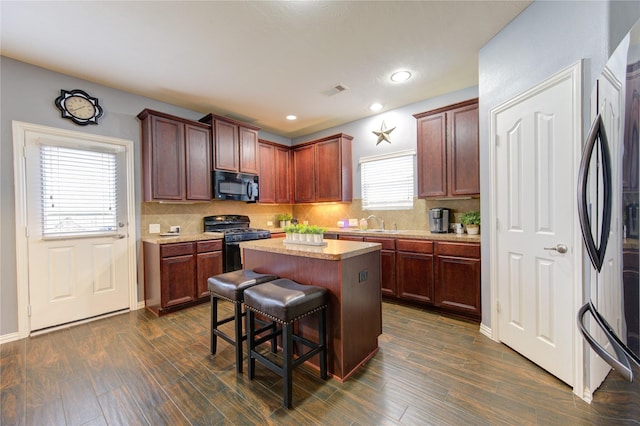 kitchen featuring a kitchen island, a kitchen breakfast bar, light countertops, dark wood-style floors, and black appliances