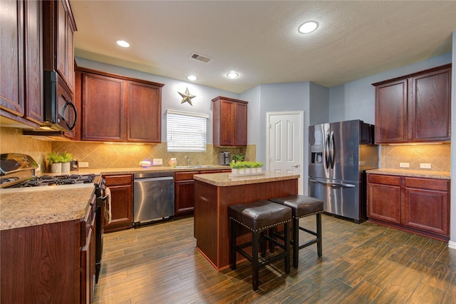 kitchen featuring visible vents, dark wood finished floors, a kitchen island, a kitchen breakfast bar, and black appliances