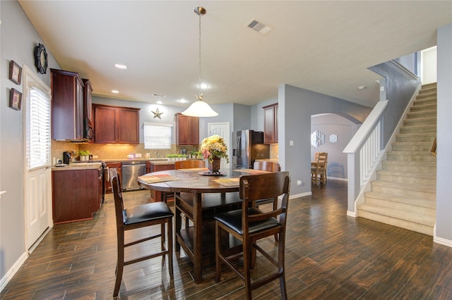 dining room featuring baseboards, visible vents, arched walkways, dark wood-style flooring, and stairs