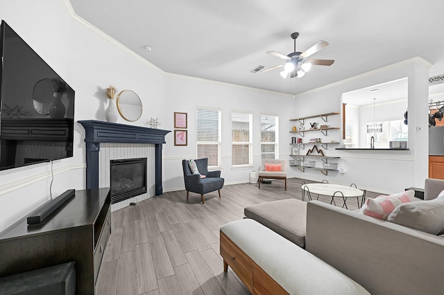 living room featuring crown molding, wood finished floors, a tile fireplace, and ceiling fan