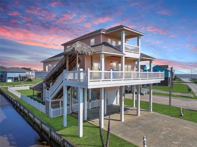 back house at dusk with a garage, a water view, a balcony, and a carport